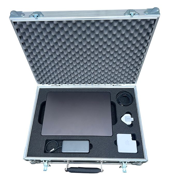 Open hard case with foam padding holding a dark laptop and charging accessories (power brick, cable, and small white adapters).